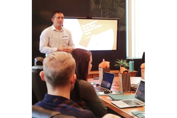 White man presents to room of people seated around a table